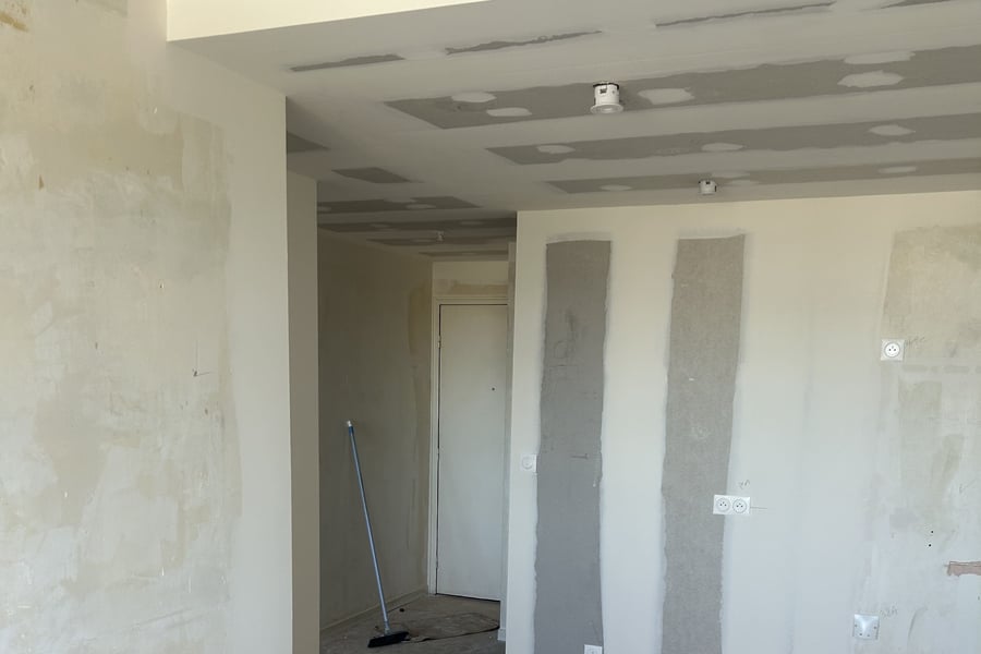 Séjour d'un appartement rennais en cours de rénovation : faux plafond en plaques de plâtre avec spots encastrés, prises neuves, enduits en cours sur les murs, sol nu