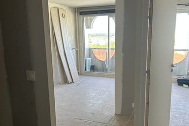 Appartement en rénovation au 13e étage à Rennes : sol nu, lames de stratifié en attente contre le mur, porte neuve et baie vitrée ouverte sur la ville