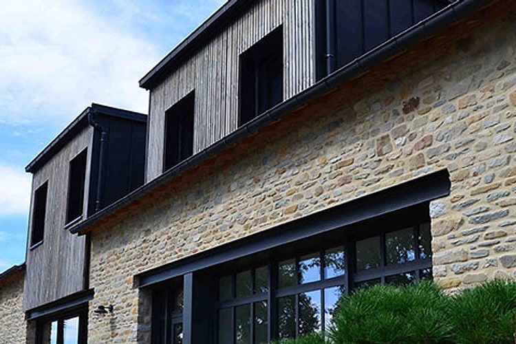 Lucarnes habillées d'un bardage bois à lames verticales de teinte gris argenté au-dessus d'une façade en pierre, maison rénovée à La Baule