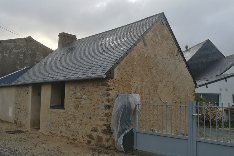 Façade en pierre rejointoyée pendant les travaux à Saint-Nazaire, pignon en cours d'enduit et poteau de portail protégé par une bâche